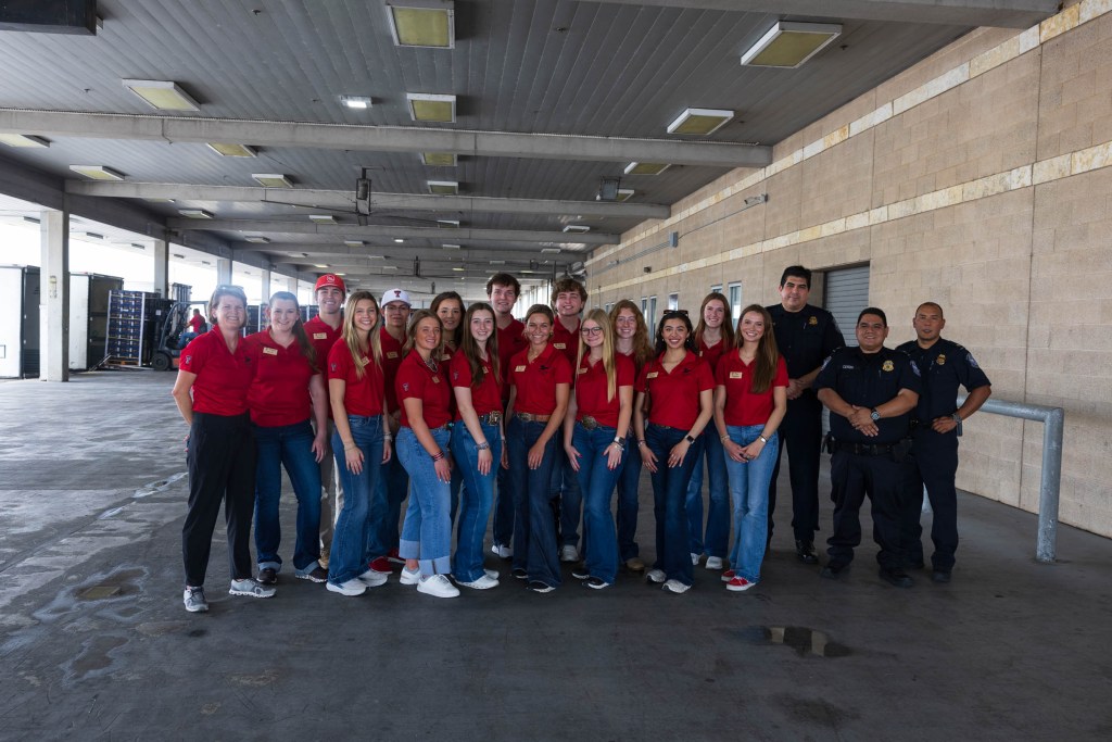 Group photo of students and staff from the Matador Institute of Leadership Engagement during their agriculture tour in the Rio Grande Valley, Texas. They are wearing matching red shirts and standing in an industrial setting.