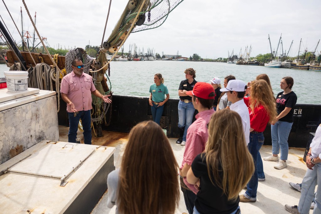 Students from the Matador Institute of Leadership Engagement listening to an instructor aboard a boat in the Rio Grande Valley, surrounded by other boats at the dock.