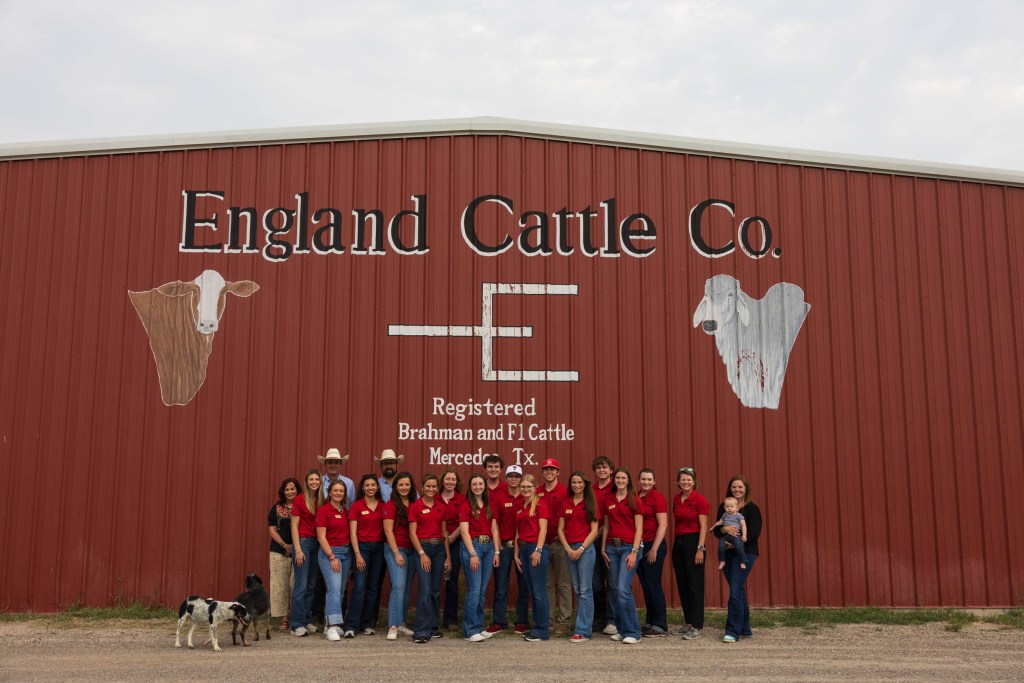 Group of students in red shirts posed in front of the England Cattle Co. building with cattle murals.