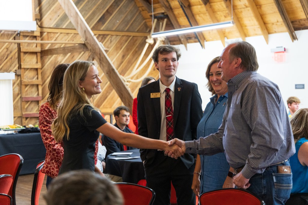 A graduate of the MILE Program shakes hands with a guest during the graduation ceremony at Texas Tech University's Dairy Barn, with onlookers in formal attire.